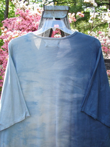 Barclay NWT Art Tee Center Script Bird Mottled Ink Sky Bronze OSFA hangs outdoors, showcasing its tunic length, drop shoulders, and three-quarter sleeves, set against a wooden fence and flowering blossoms.