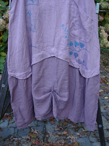 Barclay PMU Linen Explorer Jumper Pansy Lavender Size 2: A medium weight linen dress on a stand, featuring a scoop neckline, full bodice overlay, billowy lower sweep, and pansy theme paint.