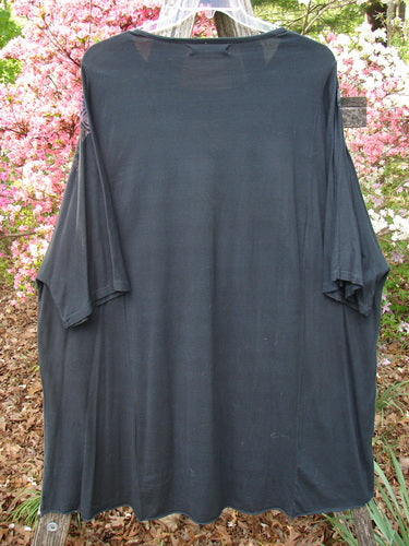Barclay Art Tunic Tee Field Friends True Black OSFA features a loose, tunic-length design with elbow-length sleeves and a wide neckline, draped on a hanger amidst vibrant azaleas.