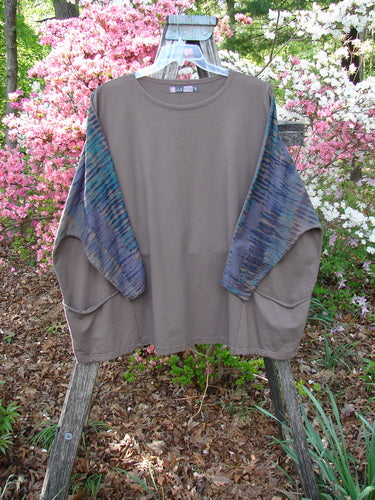 Barclay Cotton Lycra Writer's Pocket Pullover Sweatshirt hangs on a wooden stand, featuring taupe body, blue-green sleeves, dual pockets, and a unique seamless design, embodying Bluefishfinder.com's vintage, expressive style.