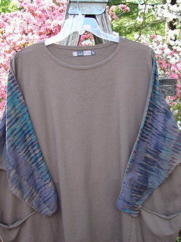 Barclay Cotton Lycra Writer's Pocket Pullover Sweatshirt features solid taupe body, sheer watercolor sleeves, dual front pockets, and rounded neckline, showcased outdoors with flowering bushes background.