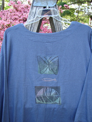1995 Silk Noile Long Sleeved Top Leaf Fish Butterfly Dusk OSFA draped on a wooden ladder, featuring block-style prints of a butterfly, fish, and geometric pattern amidst soft-focus blossoms and foliage.