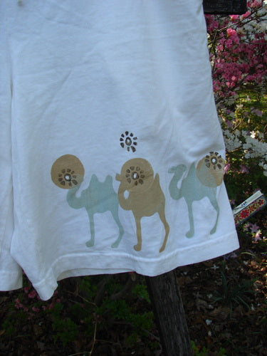 2000 Bushel Short Bus Travel Milk Size 1 displayed outdoors, featuring a whimsical camel graphic along the hem, deep front bushel pockets, full draw cord waist, and flowing mid-weight organic cotton fabric.