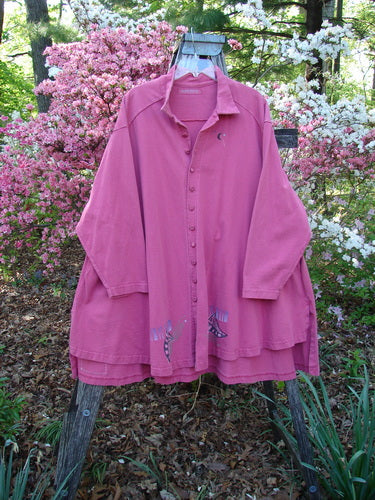 1997 Work Jacket Tiny Moon Geranium OSFA displayed on a wooden ladder in a garden, showcasing its long sleeves, button-front, flared hem with embroidery, and deep side pockets amidst blooming shrubs.