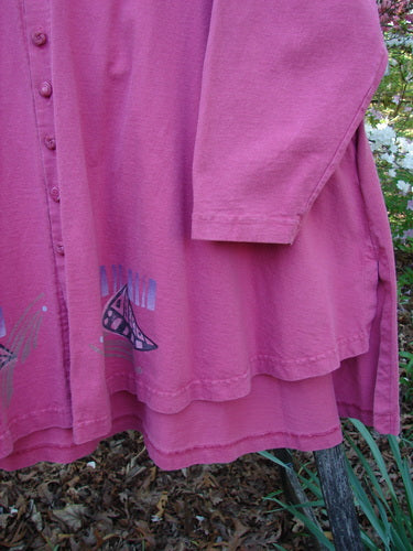 1997 Work Jacket Tiny Moon Geranium OSFA: Dusty-rose long-sleeve tunic with layered hem, featuring a small abstract print. Buttons and side pockets accentuate its design. Hangs outdoors against greenery.