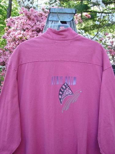 1997 Work Jacket Tiny Moon Geranium OSFA: Back view of a magenta-pink pullover with a shell-shaped graphic and NINA AND NINA text, hanging outdoors against a floral backdrop.