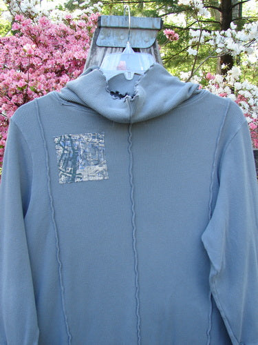 Barclay Patched Thermal Cowl Neck Roo Tunic Gray Day Size 1 on hanger, showcasing waffle thermal texture, narrow shape, curly edgings, and kangaroo pocket, set against flowering shrubs.