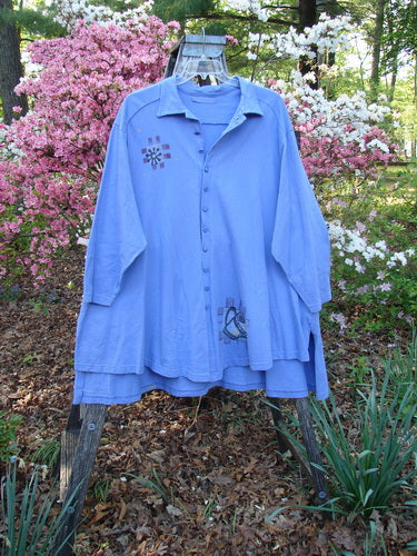 1997 Work Jacket Water Can Skylark OSFA draped on a wooden stand, showcasing its long sleeves, button-up front, embroidered designs, and double-layered panels, set against a vibrant garden backdrop.