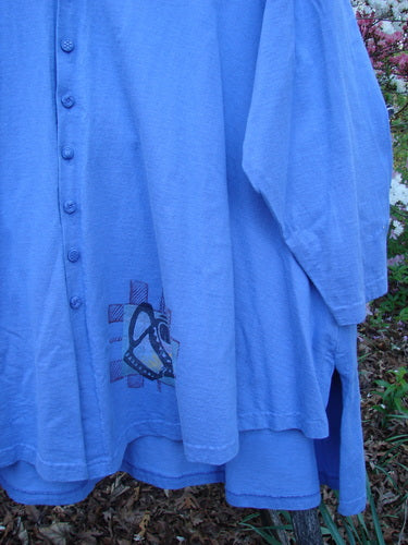 1997 Work Jacket Water Can Skylark OSFA: A periwinkle loose-fit jacket with button-front, featuring a small graphic near the hem, highlighted against an outdoor leafy backdrop.