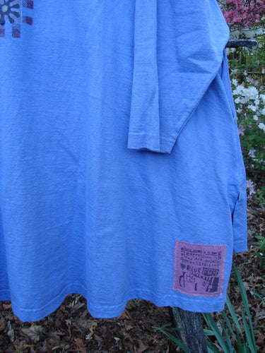 1997 Work Jacket Water Can Skylark OSFA: A light-blue, long-sleeved tunic draped over a garden chair, featuring a pink patch, textured buttons, double-layered panels, and vented sides, embodying vintage charm.