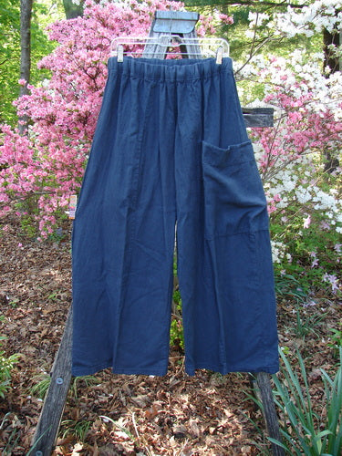Barclay Heavy Linen Single Side Pocket Pant Unpainted Navy Generous Size 0 displayed on a hanger outdoors, featuring an elastic waistband and single patch pocket, highlighting a relaxed, flowing design against a garden backdrop.