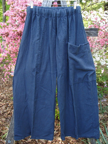 Barclay Heavy Linen Single Side Pocket Pant Unpainted Navy Generous Size 0 displayed on a hanger, showcasing wide legs, elastic waistband, and a large patch pocket, set against flowering shrubs.
