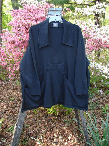 Dark-navy 2000 Interlock Peat Bog Top Unpainted Black Size 2 hangs on a wooden stepladder, featuring a deep V-neck, broad collar, long sleeves, kangaroo pocket, surrounded by garden shrubs.