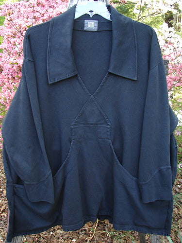 The 2000 Interlock Peat Bog Top Unpainted Black Size 2 features a loose fit, deep V-neck, drop shoulders, and a large kangaroo pocket, expertly showcased outdoors on a hanger.