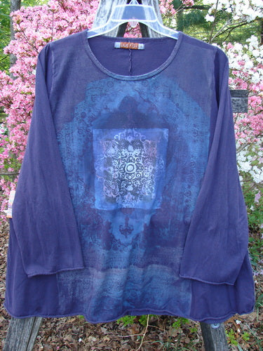 Barclay Long Sleeved A Line Tee Celtic Journey Purple Royal Size 1 features a mandala design in blues and purples, long sleeves, and a flared hem, hanging against flowering shrubs.