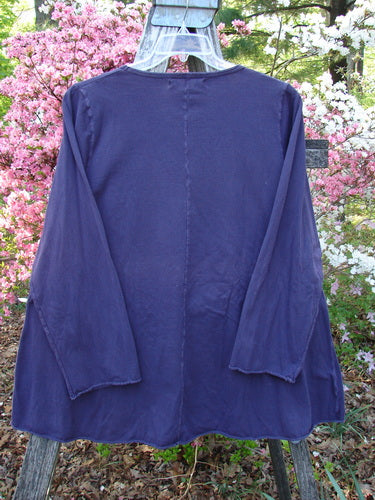 Barclay Long Sleeved A Line Tee Celtic Journey Purple Royal Size 1 hangs outdoors, showcasing its rounded neckline, swinging A-line shape, and cozy long sleeves against a backdrop of flowering shrubs.
