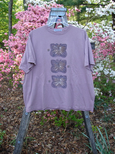 1996 Short Sleeved Tee Triple Butterfly Petal Size 2, displayed on a wooden easel, features three vertical butterfly motifs, exemplifying Bluefishfinder.com's vintage style with its square shape and ribbed neckline.