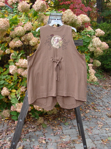 Image alt text: "1997 Merchant Vest with floral spin design on wooden stand, part of the Holiday Collection in Mandola. A-line shape, diamond cut buttons, rear tunnel tab, and shorter scoop hemline. Made from organic cotton."