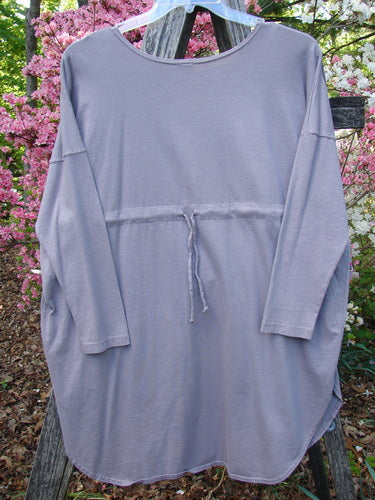 Barclay Long Sleeved Pop Top Celtic Spirograph Stone Size 1 hangs outdoors, showcasing its loose fit, dropped shoulders, rounded hem with side vents, tie-string waist, and oversized front pocket with textured button.