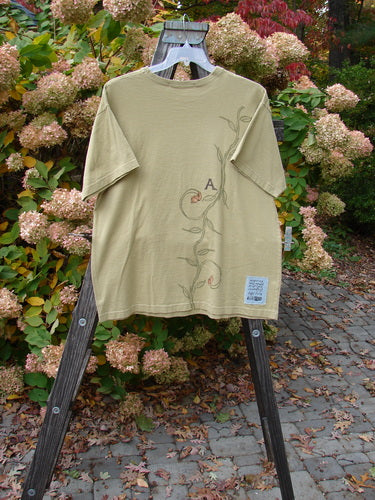 1998 Botanicals Short Sleeved Tee Continuous Vine Seed Size 1 displayed on a wooden easel, showcasing its floral design and ribbed neckline, crafted from medium-weight organic cotton.