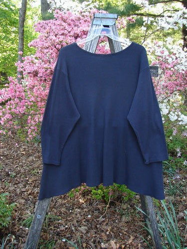 Barclay Thermal A Lined Tunic Top Paisley Graph Black Size 2 hangs on a rustic wooden ladder, showcasing its long sleeves, rounded neckline, and sweeping hemline amidst a vibrant garden backdrop.