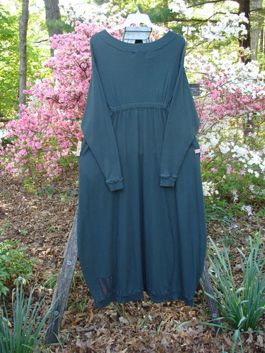 Barclay Patched Thermal Curve Dress Forest Size 2 displayed outdoors, showcasing a unique figure-eight shape with exterior stitchery and double ribbed details, against a garden backdrop with flowering shrubs.