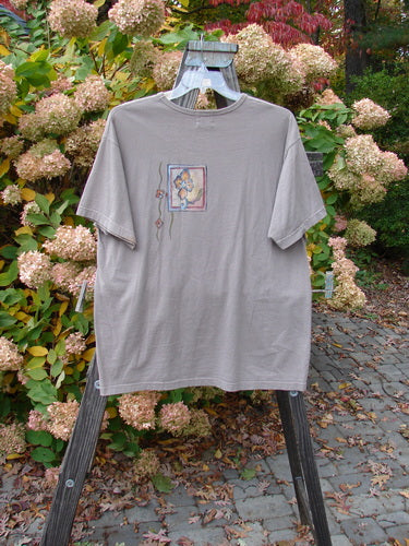 1999 Short Sleeved Tee Circle Bloom Shale Size 1 displayed on a hanger, featuring a slightly rolled ribbed neckline, straight shape, and floral-themed paint design, made from medium weight organic cotton jersey.