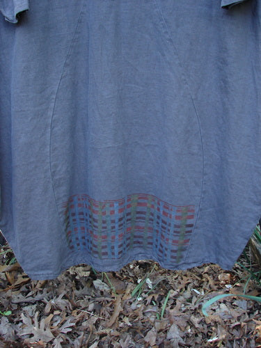 Barclay Linen Tea Ceremony Thostle Dress features a curved seam pocket and multicolored grid hem, crafted in heavier weight linen, showcasing BlueFishFinder's vintage style. Scattered oak leaves accentuate its outdoor elegance.