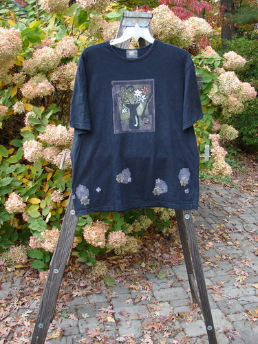 2000 Artist Choice Short Sleeved Tee Floral Vase Black Size 1, displayed on a rack, featuring a cat and flowers painting on the front, straight shape, and rolled ribbed neckline.