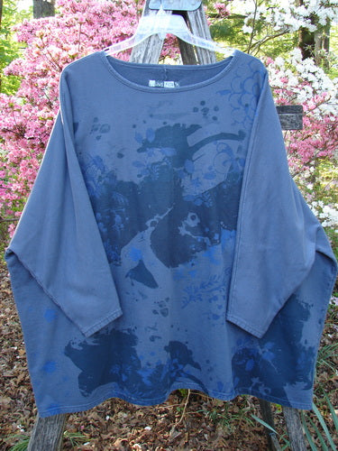 Barclay Fleece Big Square Pullover Botanical Path Night Navy OSFA, showing a loose-fitting tunic-style with dolman shoulders and narrowing sleeves, hangs from a wooden A-frame amidst azaleas.