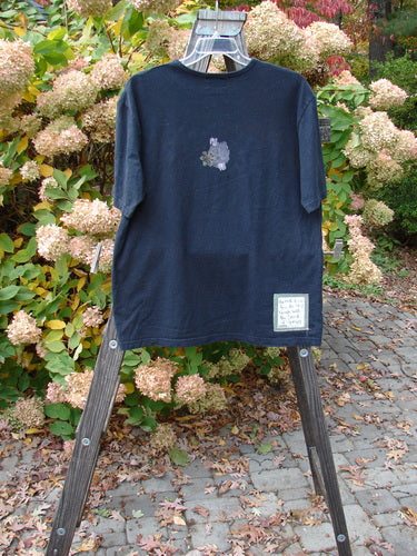 2000 Artist Choice Short Sleeved Tee Floral Vase Black Size 1 displayed on a wooden ladder, showcasing its floral vase design and medium weight organic cotton jersey fabric.