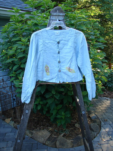 2000 Hemp Cotton Shorty Jacket Tri Rake Blue Jet Size 1 displayed outdoors on a swing, showcasing its rounded neckline, longer sleeves, curved panels, and four shell button closure.