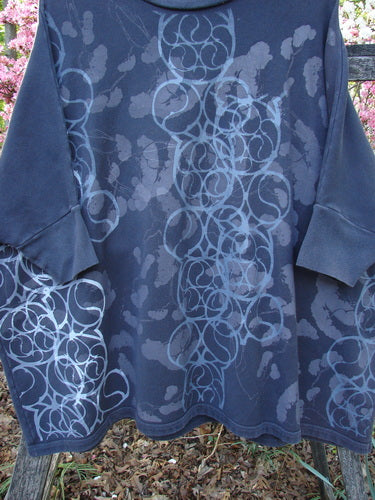 Barclay Fleece Banded Sleeve Dolman Top Continuous Spirograph Black OSFA draped outdoors, showcasing its wide, boxy shape and overlapping circle pattern, with pink blossoms softly framing the scene.
