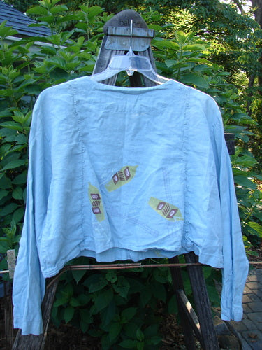 2000 Hemp Cotton Shorty Jacket in Blue Jet, showcasing its sweet widening and rounded hem, vertical curved sectional panels with tiny loops, and four-shell button closure, displayed on a hanger.