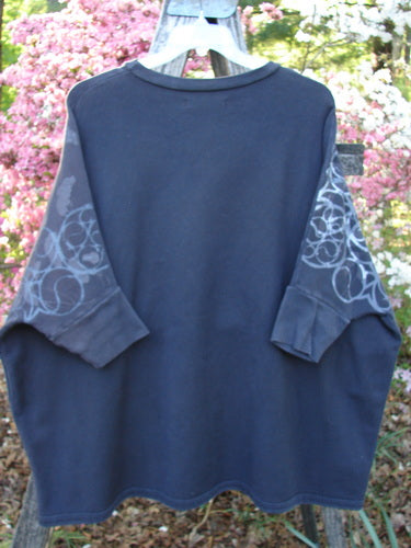 Barclay Fleece Banded Sleeve Dolman Top Continuous Spirograph Black OSFA is displayed on a hanger, featuring a wide boxy shape, spirograph-patterned sleeves, in a cozy outdoor garden setting.
