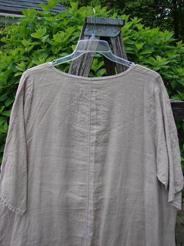 Barclay Lightweight Linen Tea Time Top Unpainted Rice Paper Size 2, a loose-fitting tunic with three-quarter sleeves, hanging on a ladder, showcasing its flowy A-line shape and rounded neckline.