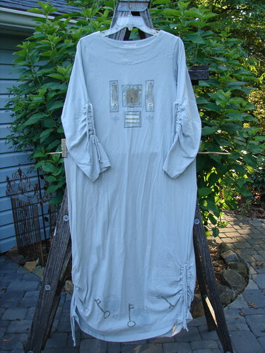 1999 Starlight Dress Celtic Garden Blue Horizon Size 0 displayed on a clothes rack, showcasing its long shape, softer rolled neckline, and sleeve lacings with intricate Celtic Garden paint details.
