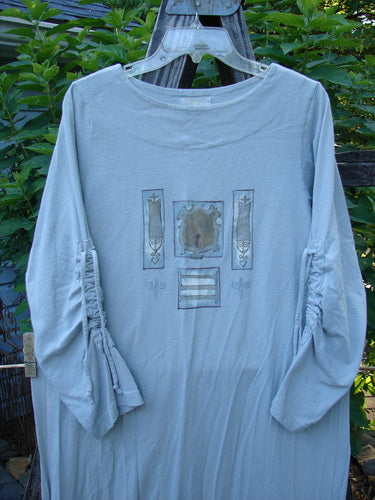 1999 Starlight Dress Celtic Garden Blue Horizon Size 0 on a clothes rack, featuring long sleeves, a rolled double-layered neckline, sleeve lacings, and Celtic garden paint accents.