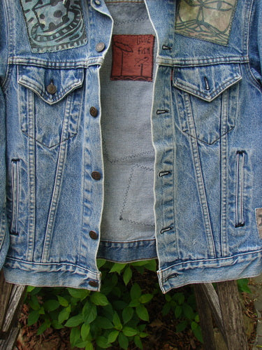 1995 Patched Levi Strauss & Co Denim Blue Jean Jacket Kitty Kitty Stone Wash Size 0 draped on a chair, showcasing front flap pockets, metal buttons, and unique patches against a garden backdrop.