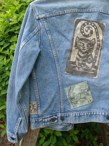 1995 Patched Levi Strauss & Co Denim Blue Jean Jacket, featuring three stylized cat patches, draped over a rail. Showcases vintage charm with classic details and artistic feline-themed embellishments.