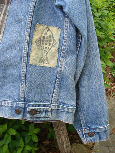 1995 Patched Levi Strauss & Co Denim Blue Jean Jacket Kitty Kitty Stone Wash Size 0, featuring a fish motif patch, displayed on a wooden post in a leafy outdoor setting.