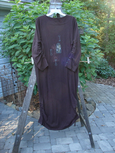 1999 Starlight Dress Celtic Key Deep Burgundy Size 0 on a clothes rack, showcasing a longer shape with sleeve lacings, vertical drawcord accents, and a unique shimmer paint design.