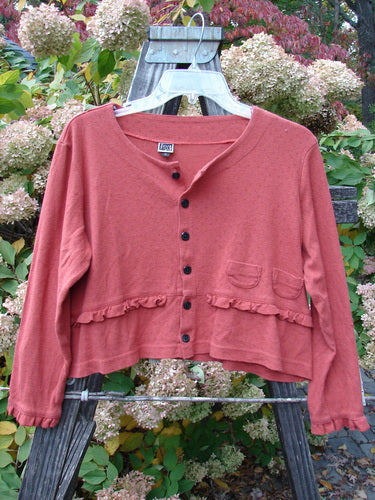 2000 Wool Pointelle Annu Jacket in Bittersweet on a hanger, showcasing flared crop shape, lettuce-edged accents, two front pockets, and painted buttons.