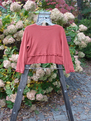 2000 Wool Pointelle Annu Jacket Unpainted Bittersweet Size 0: A red sweater on a wooden rack, featuring a flared slightly crop shape, lettuce edged accents, and two front rounded pockets.