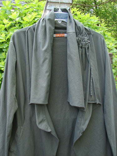 Barclay Cotton Lycra Gather Collar Open Front Jacket Unpainted Forest Size 1 displayed outdoors, showcases waterfall-style lapels and ruched shoulder detail, reflecting Bluefishfinder.com's vintage-inspired, creatively expressive clothing line.