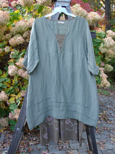 Barclay Hemp Silk Triangular Two Tier Dress in Soft Moss Rock with garden-themed painted lower skirt and pinched accents, displayed on a rack.