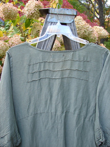 Barclay Hemp Silk Triangular Two Tier Dress on a wooden stand, featuring a V-shaped neckline, pinched accents, three-quarter sleeves, and a garden-themed lower skirt.