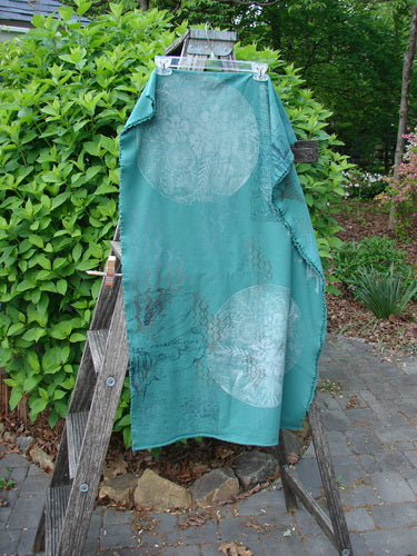 The Barclay Heavy Weight Organic Sweatshirt Art Wrap Moon Garden Emerald OSFA is draped over an outdoor ladder, showcasing its generous shape and curly edgings, enhanced by abstract script designs.