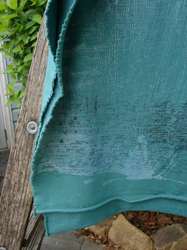 Barclay Heavy Weight Organic Sweatshirt Art Wrap Moon Garden Emerald OSFA draped over a weathered wooden bench, showcasing its distressed hem and scribble-style print, with a backdrop of natural elements.