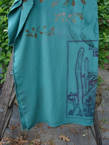 Barclay Heavy Weight Organic Sweatshirt Blanket Pony Garden Emerald OSFA draped over a wooden trellis, showcasing leaf motifs and a cactus panel, with raw cut edges, suitable as decor or wrap.